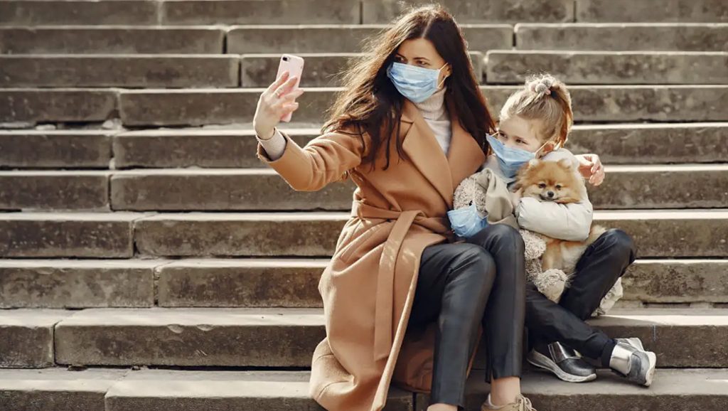 Woman and child in protective masks taking a selfie with a dog outside on some steps.