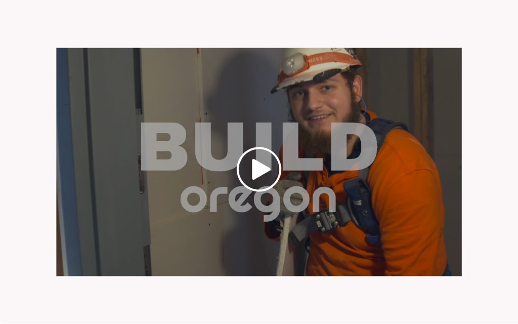 Construction worker smiling with Build Oregon logo and play button overlaid.