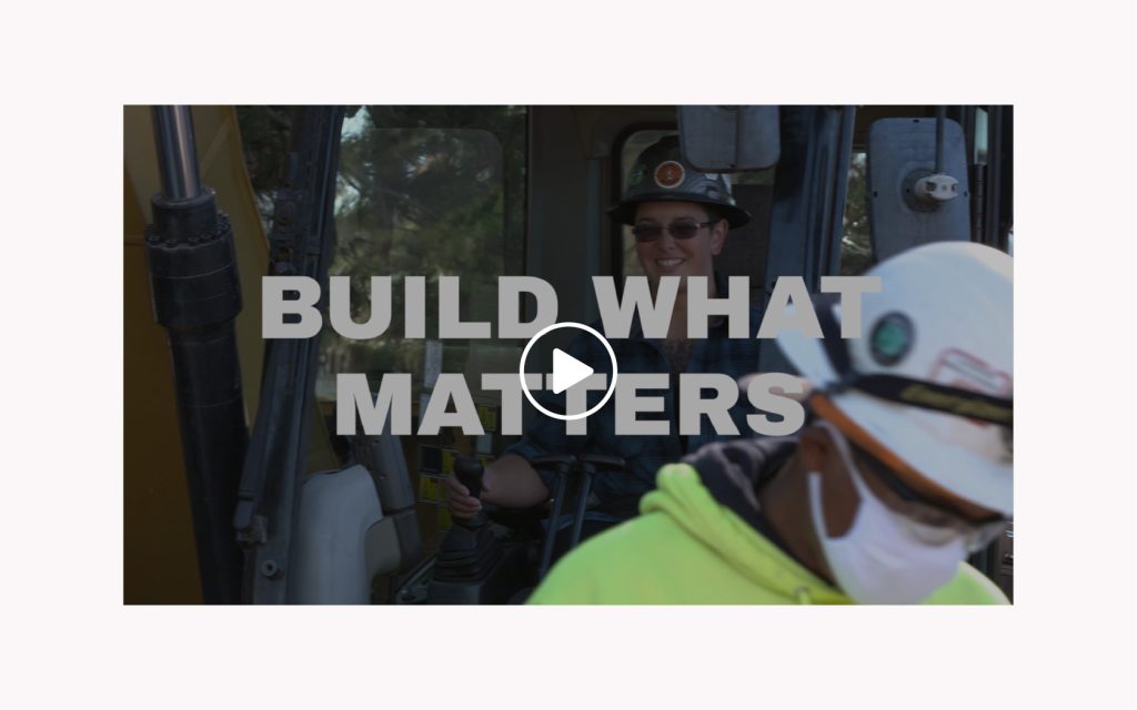 Construction workers outside with masks, with the words "Build What Matters" and a play button overlaid.