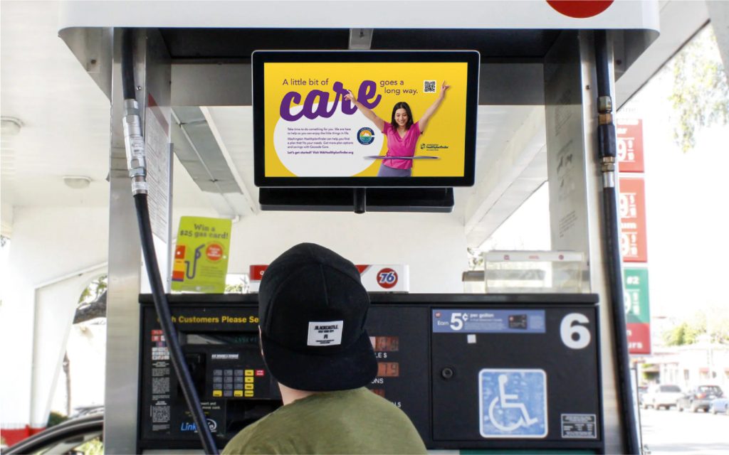 A person at a gas pump looks at a Washing Health Benefit Exchange ad on a monitor.