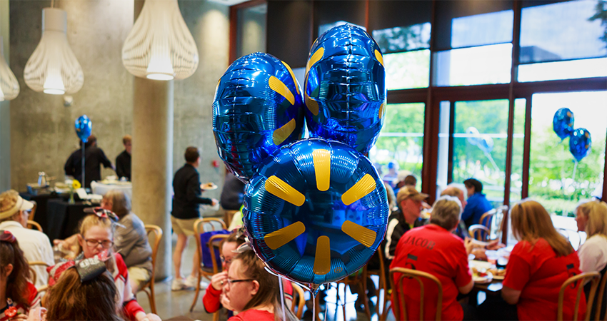 People at a celebratory event sitting and eating with Walmart balloons in the foreground.